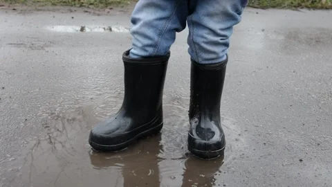 Child in rubber boots stomps in a puddle, mud splashes. slow motion video Stock Footage 220734910