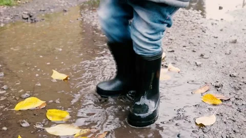 Child in rubber boots stomps in a puddle, mud splashes. slow motion video Stock Footage 220734945