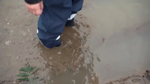 A child in rubber boots walks through a deep muddy puddle after rain Stock Footage 285618679