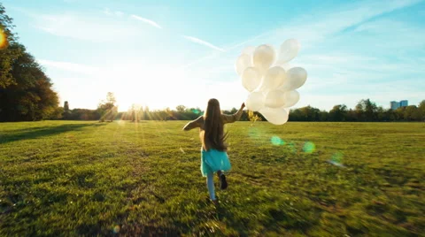 Child running across the field and holding her balloons Stock Footage