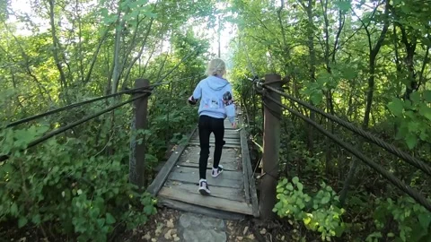 The child runs along the path and reaches the hanging wooden bridge over the Vídeos de archivo 145967672