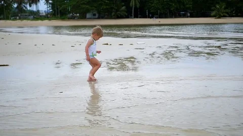 The child runs gleefully along the beach, creating a spray of water Vidéo 74397448