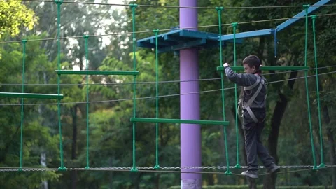A child in safety gear navigating high obstacle ropes course and ladders  Stock Footage 345285591