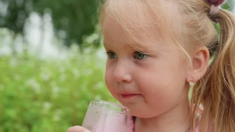 Child sampling pink drink outdoors, Young girl tasting juice in sunny field Stock Footage 329499098