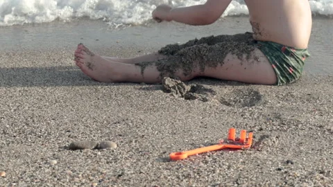Child on sands beach digging or throwing wet sands on feet Video stock 218822647
