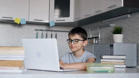 The child the schoolboy learns lessons being at home sitting in the kitchen at Video stock 127927778