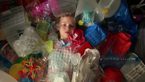 A child schoolgirl is lying in a pile of multi-colored garbage, a plastic bag Stock Footage 106984144