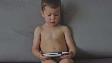 Child seated on couch absorbed in handheld gaming console illustrating fun and Stock Footage 284673474
