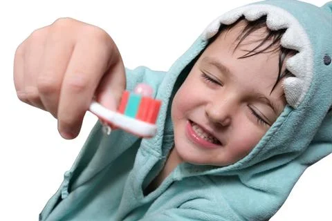 Child in shark bathrobe brushing teeth with toothbrush and toothpaste. Studio Stock Photos