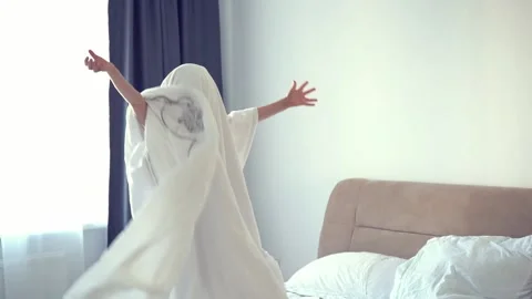 A child in a sheet plays ghost in the bedroom on the bed. halloween Stock Footage 224690524