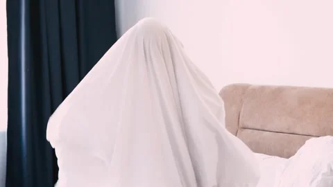 A child in a sheet plays ghost in the bedroom on the bed. halloween Stock Footage 224690570