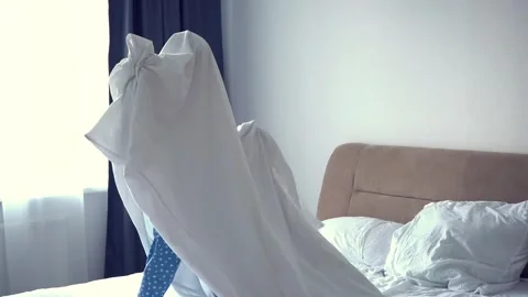 A child in a sheet plays ghost in the bedroom on the bed. halloween Stock Footage 250956836