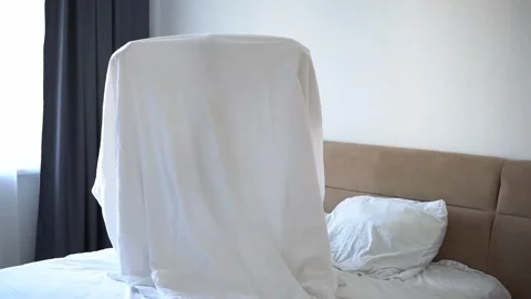 A child in a sheet plays ghost in the bedroom on the bed. halloween 스톡 동영상 250956919