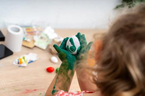 Child shows Easter egg decoration with green paint on hands during springti.. Foto stock