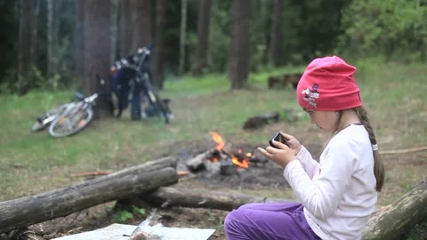 Child sit by fire plays on a smartphone. Bonfire athletic posture. Stock Footage 113351165