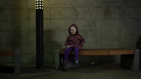 The child sits on a bench under the light of a lantern at night in the park. Stock Footage 89592663