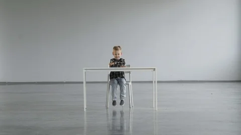 The child sits on chair at the tables and turns his head in different directions Stock Footage 124941953