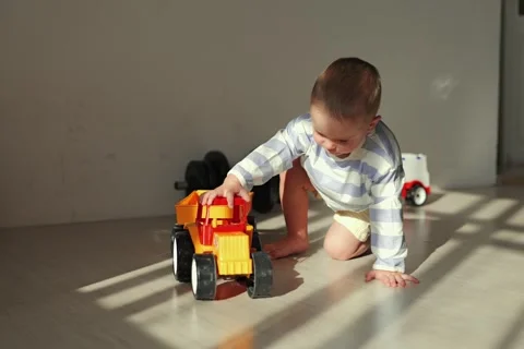 A child sits on the floor and plays with toy trucks and cars. Shadows from the Stock Footage 336445919
