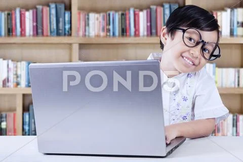 Child Sits In The Library With Laptop