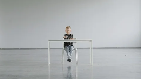 The child sits motionless on a chair at the table and looks at the camera Stock Footage 124941973