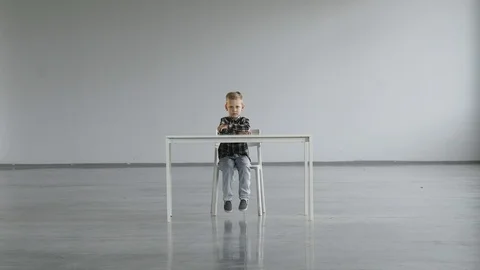 The child sits motionless on a chair at the table and looks at the camera Stock Footage 124942011