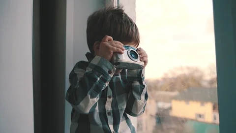 The child sits near the window with a camera in his hands Stock Footage 129098747
