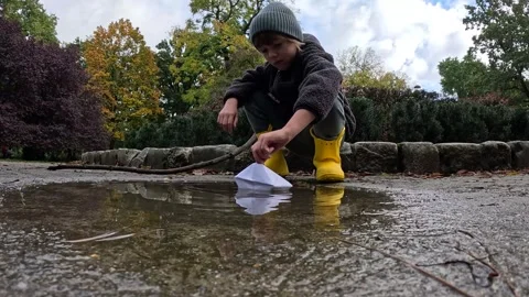 Child Sits by a Puddle, Playing with Paper Boats on a Cold Autumn Day Stock Footage 254080251