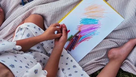 A child sits on a soft blanket in a grassy area, using crayons to create Stock Footage 341490895