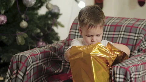 The child sits under the Christmas tree and opens his gift 動画素材 112180235