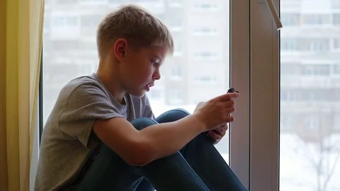 The child sits on the windowsill and looking at smartphone 库存影片 70377537