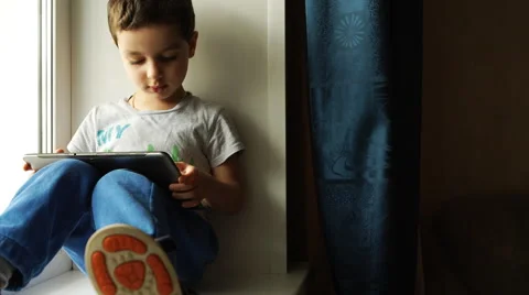 Child sits on a windowsill with a tablet pc Vídeo Stock 50593939
