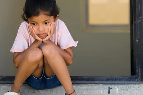 Child sitting alone on a windowsill, lost in thought during a warm afternoo.. Stock Photos