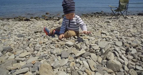 The child is sitting on the beach and playing with stones. Stock Footage 89929294