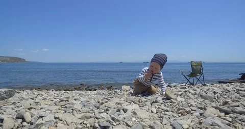 The child is sitting on the beach and playing with stones. Видео 89929299