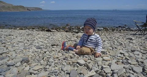 The child is sitting on the beach and playing with stones. Видео 89929376