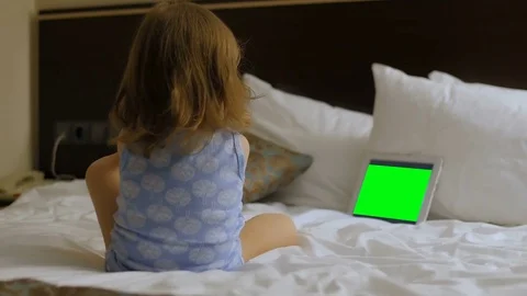 A child is sitting in the bedroom on the bed looking at the phone, tablet Stock Footage 75345006