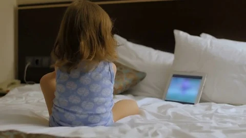 A child is sitting in the bedroom on the bed looking at the phone, tablet Stock Footage 75405988