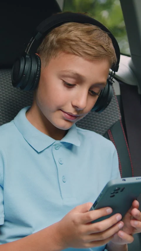 Child sitting in car and using smart phone and headphones. Attaractive little bo Stock Footage 333588365