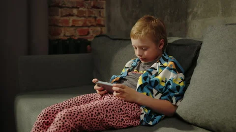 Child is sitting on the couch and playing on the phone with an emotional face Stock Footage 200990213