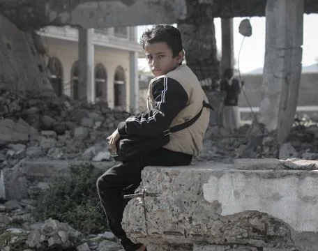A child sitting in front of a destroyed school Stock Photos