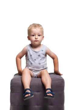 Child sitting on a gray cube in a simple setting wearing casual clothes Stock Photos