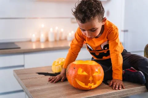Child sitting at kitchen table dressed as pumpkin playing with decorated Stock Photos