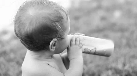 Child sitting on the lawn and drinking milk from a bottle. Video stock 50259809