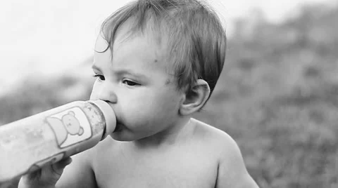 Child sitting on the lawn and drinking milk from a bottle. Stock Footage 50260141