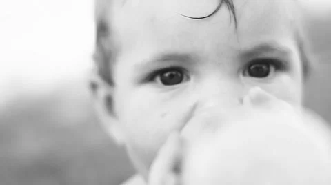 Child sitting on the lawn and drinking milk from a bottle. Video stock 50260357