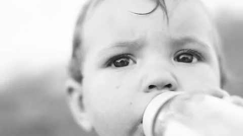 Child sitting on the lawn and drinking milk from a bottle. Stock Footage 50260511