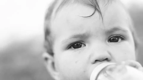 Child sitting on the lawn and drinking milk from a bottle. Video stock 50260552