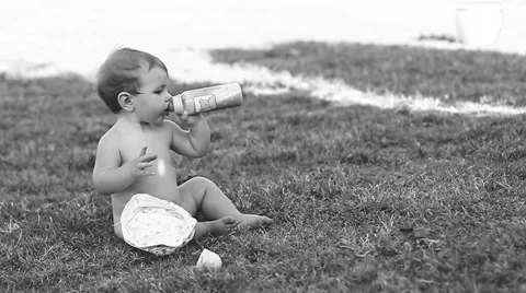 Child sitting on the lawn and drinking milk from a bottle. 스톡 동영상 50260623