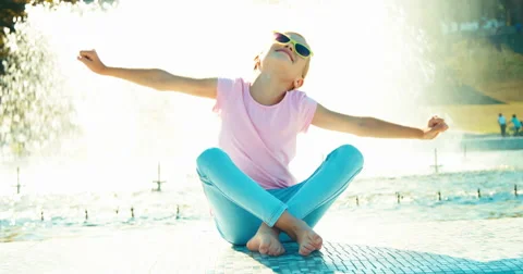 Child sitting near fountain at sunny day and stretching Stock Footage