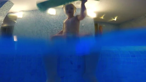 The child is sitting on the nosing of the pool and playing with the foam stick Stock Footage 106483492
